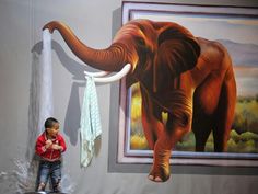 a young boy standing in front of a painting of an elephant