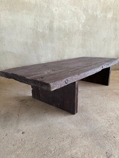 a wooden bench sitting on top of a cement floor next to a white stucco wall