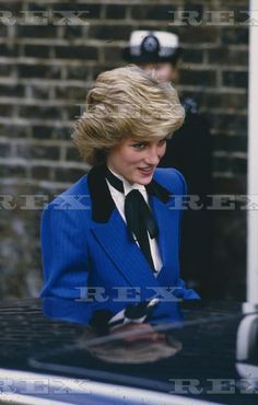 the woman is wearing a blue suit and black tie, standing in front of a police car