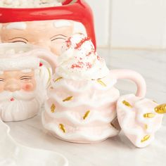 two ceramic santa mugs sitting next to each other on a white counter top with gold accents