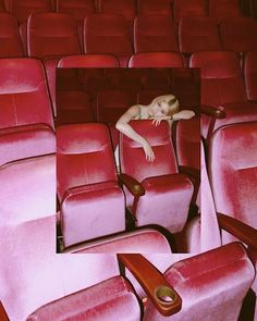 there is a woman sleeping in the middle of an empty theater seat with her head resting on the armrests