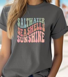 This Tee exudes a coastal vibe with its Saltwater, Seashells, Sunshine design, perfect for those who love the beach and summer. It is a versatile piece that can be worn casually or layered for a more stylish look. Ideal for beachgoers, summer lovers, and those who enjoy the laid-back lifestyle. Perfect for vacations, beach days, and outdoor gatherings. Product features - Ribbed knit collar for elasticity - Made from smooth, strong fabric - Medium fabric for year-round comfort - Ethically and sustainably made - Plus Sizes Available - Sizes: S-5XL - More Colors and Kids Sizes Available - Message Me If You're Interested  Care instructions - Machine wash: warm  - Non-chlorine: bleach as needed - Tumble dry: medium - Do not iron - Do not dryclean Beach Slogan Tops For Beach Season, Beach Slogan Tops, Beachy Crew Neck Top With Screen Print, Beachy Crew Neck Surfing Tops, Crew Neck Surfing Tops For Vacation, Pre-shrunk Tops For Surfing During Beach Season, Beachy Crew Neck Top For Surfing, Beachy Printed Crew Neck Tops, Beachy Crew Neck Printed Tops