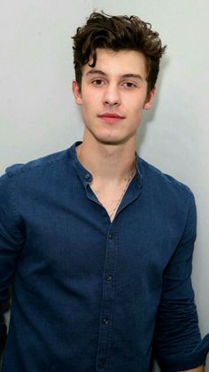 a young man in a blue shirt is posing for the camera with his hands on his hips