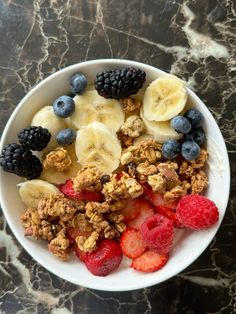 a bowl filled with granola, berries and kiwis on top of a marble table