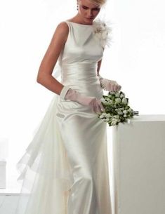 a woman in a white wedding dress holding a bouquet and standing next to a wall