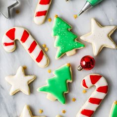 christmas cookies decorated with icing and candy canes on a marble countertop next to cookie cutters