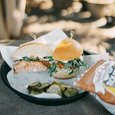 a plate with a sandwich and pickles on it sitting next to a bag of chips