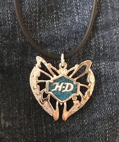 This silver Harley Davidson butterfly pendant is inlaid with turquoise and has the HD in silver on the front.    It also has the HD trademark on the back and pendant is approximately 1" high by 1&1/4" wide and is on a 4mm rubber cord, with the cord being about 16 - 18" and having a sterling silver clasp, better cord for those with metal allergies.  There is a 4" length of chain added to make it adjustable to individual taste The end of the cord by the clasp is small enough for you to add other b Silver Stamped Heart Pendant Jewelry, Silver Engraved Butterfly Jewelry, Blue Stamped Jewelry For Gifts, Blue Stamped Jewelry For Gift, Silver Heart Jewelry With Butterfly Charm, Silver Butterfly Jewelry For Collectors, Silver Jewelry With Butterfly Charm For Anniversary, Turquoise Butterfly Sterling Silver Jewelry, Wire Earrings