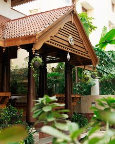 a wooden gazebo surrounded by greenery in front of a building