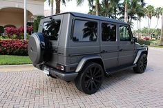 a mercedes benz g - class is parked in front of a palm tree lined driveway