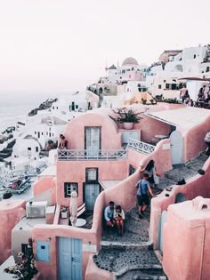 people are walking up the steps to some buildings on the cliff above the water in front of them