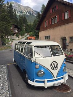 a blue and white vw bus parked in front of a building with mountains in the background