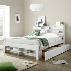 a white bed with drawers underneath it and a green pillow on the floor next to it