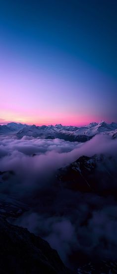 the sun is setting over some mountains covered in low lying clouds and fog, as seen from an airplane