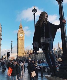 a woman is standing on the street in front of big ben, with her arms outstretched