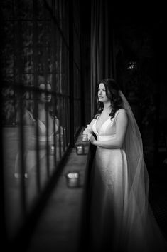 a woman in a wedding dress standing next to a window with her arms crossed and looking at the camera