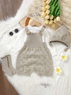 a baby's sweater and hat are laying on a fur rug next to flowers