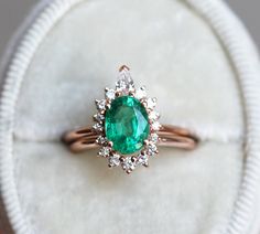 an emerald and diamond ring is displayed on a white velvet surface with a circular cloth