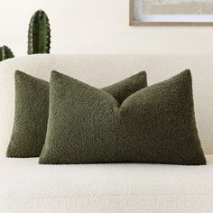 two green pillows sitting on top of a white couch next to a cacti