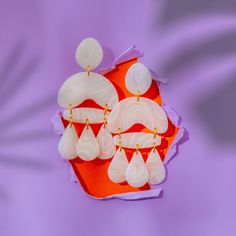 two pairs of white earrings sitting on top of an orange box with purple paper in the background