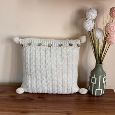 a white pillow sitting on top of a wooden table next to a vase with flowers