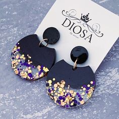 two pairs of black and gold earrings with confetti on the bottom, one is shaped like an earring