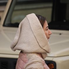 a woman with a hood on her head is walking down the street in front of a car