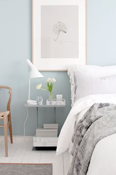 a bedroom with blue walls and white bedding has a small table with flowers on it