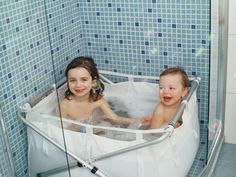 two young children in a bathtub with bubbles on the wall and blue tiled walls