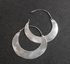 Super sleek silver hoop earrings handmade in Cairo using traditional silversmithing techniques. I've taken the shape of a typical Nubian or bedouin earring but have left it plain without the usual etched designs. This creates a clean, quite minimalist earring which is unusual and very wearable. They also catch the light beautifully. Available in 3 sizes - width 3.2cm, 4.5cm and 5.2cm Cairo hallmarks Small: Weight: 1.4gm Width: 3.2cm Length: 3.3cm Medium: Weight: 2.5gm Width: 4.5cm Length: 4.1cm Hoop Earrings Handmade, Minimalist Earring, Raw Gemstone Ring, Funky Earrings, Etched Designs, Wide Band Rings, Raw Gemstones, Ethnic Jewelry, Crystal Rings