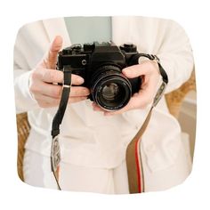 a person holding a camera in front of their face with both hands and wearing a white coat