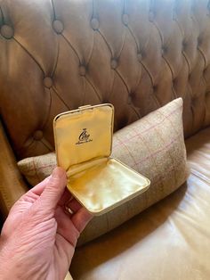 a person holding an open ring box in front of a brown leather couch with pillows