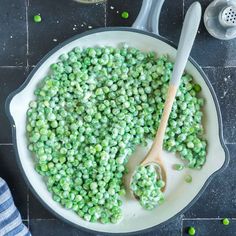 peas being cooked in a skillet with a wooden spoon and measuring cup next to it