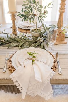 the table is set with white linens, silverware and greenery on it