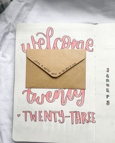 an open notebook with a brown envelope and pink lettering on the cover that says welcome twenty - three