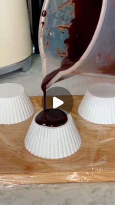 chocolate sauce being poured into white plastic cups on a cutting board with other items in the background