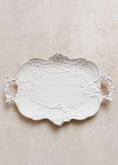 a white tray with ornate designs on the bottom and sides, sitting on a beige surface