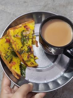 two pieces of pizza on a metal plate with a cup of tea in the middle