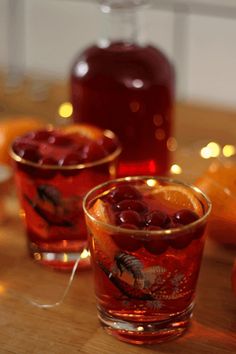 two glasses filled with liquid sitting on top of a wooden table next to oranges