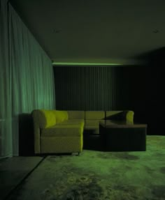 a couch and ottoman in a dark room with curtains on the wall, green light coming from behind