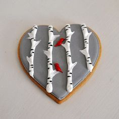 a heart shaped cookie decorated with white birch trees and red cardinals on it's side