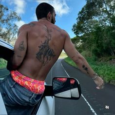 a man with tattoos on his back leaning out the window of a car