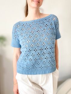 a woman standing in front of a white wall wearing a blue crochet sweater