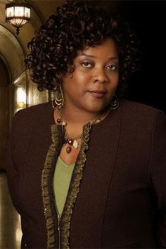 a woman with curly hair standing in front of a door and looking at the camera