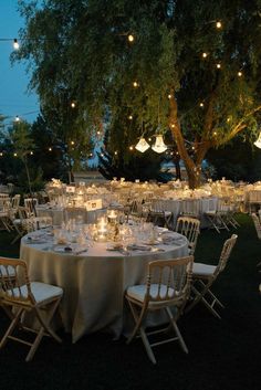 an outdoor dining area with tables and chairs, lit by string lights hanging from the trees