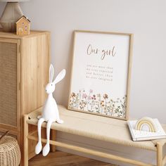 a white rabbit sitting on top of a bench next to a wooden cabinet and lamp