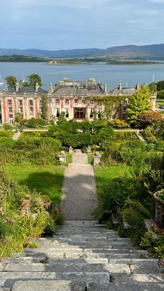 an old mansion with stone steps leading up to the front yard and gardens surrounding it