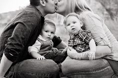 a man and woman kiss their children while they sit on the ground