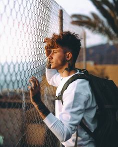 a man leaning against a fence with his hand on the chain link fence