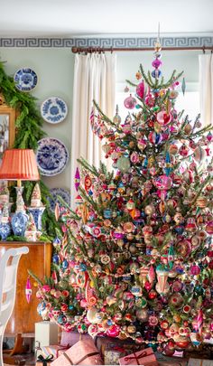 a brightly colored christmas tree in a living room with ornaments on the wall behind it